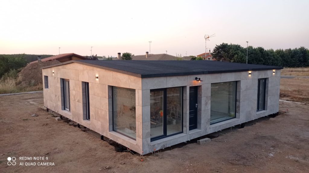 Casa modular con fachada de piedra en su parcela al atardecer